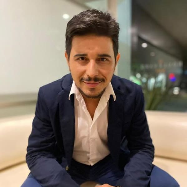 Homem sorrindo usando terno, sentado em sofá.